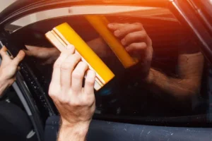 Professional window tinting installation on a sleek black car under bright sunlight, showcasing the reflective and protective properties of tinted windows