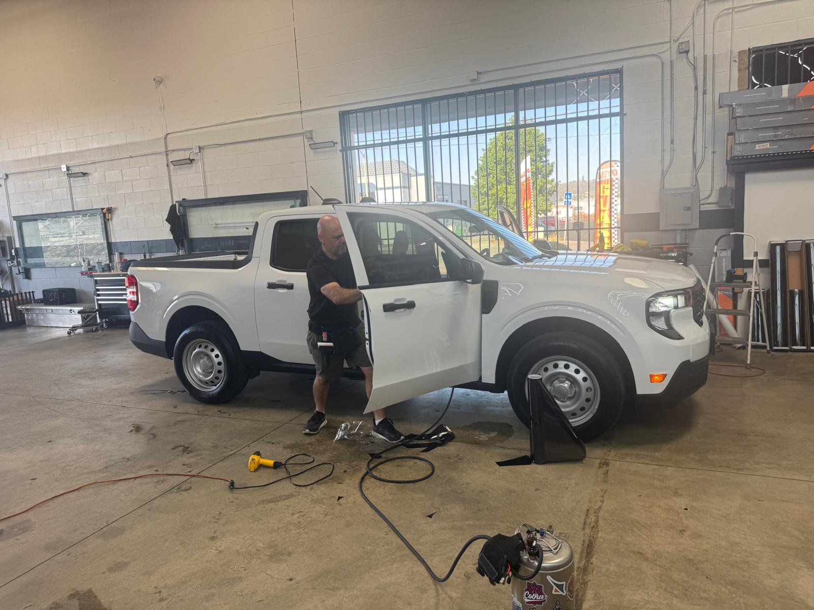 Cali Auto Glass and Tint technician installing window tint film on a Ford Maverick truck door in the El Cajon shop